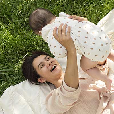 Mother lifting a baby while lying on the grass