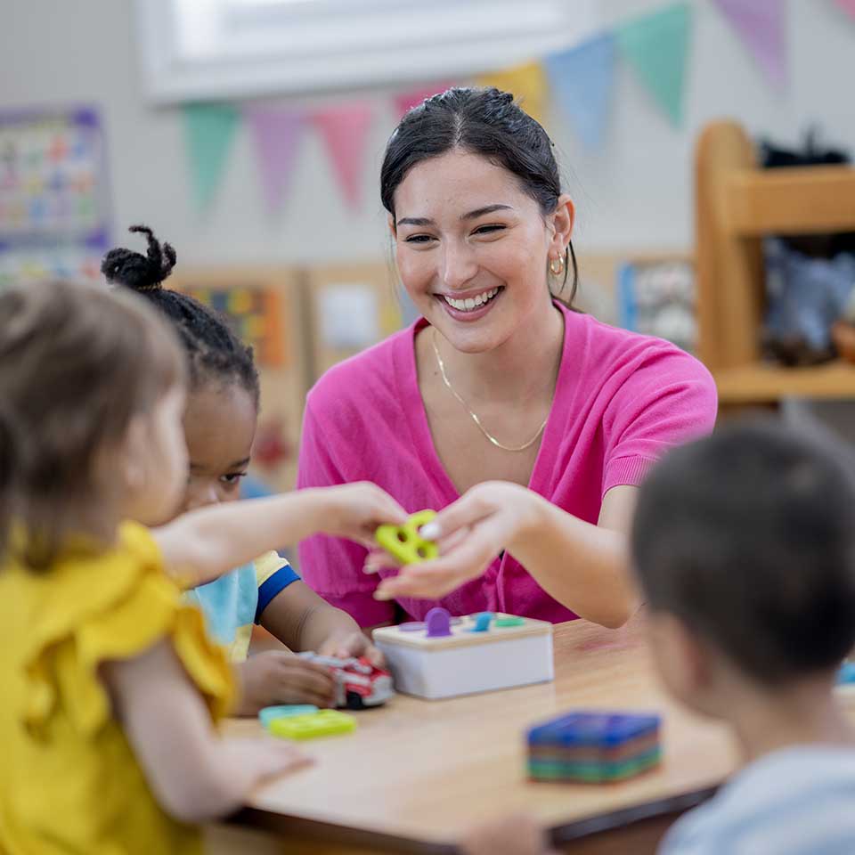 Nevada ECAC Reports and Documents Strategic Plan Framework Caregiver helping children with a classroom activity